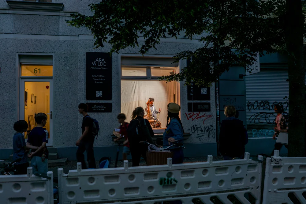 Passers-by outside the illuminated Forderfenster at dusk